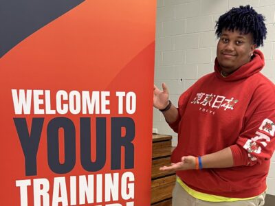 Peer Leader stands next to training camp sign