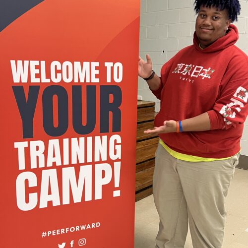 Peer Leader stands next to training camp sign