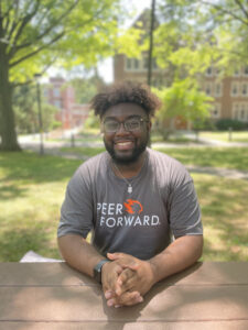 Young man in a grey PeerForward shirt smiling at camera