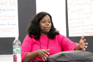 A woman in a pink shirt in a classroom addressing a room.
