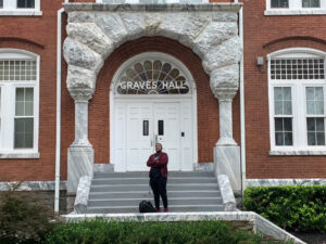 A young man standing in front of a building with the sign "Graves Hall" above it.