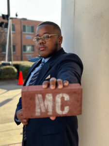 A young man holding a brick that read "MC" facing towards the camera. 