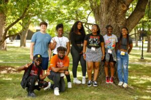 A group of young adults smiling at the camera standing under a tree.