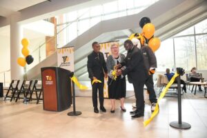 Three adults gather together to cut a ribbon at a ribbon cutting ceremony. 