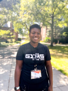 Jaliza Collins standing on a sidewalk surrounded by trees and smiling at the camera. 