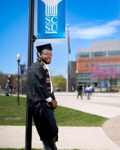 Young man in graduation garb posing on the Southern Connecticut State University campus