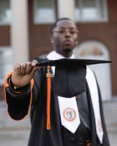 a young man holding a graduation cap up to the camera.
